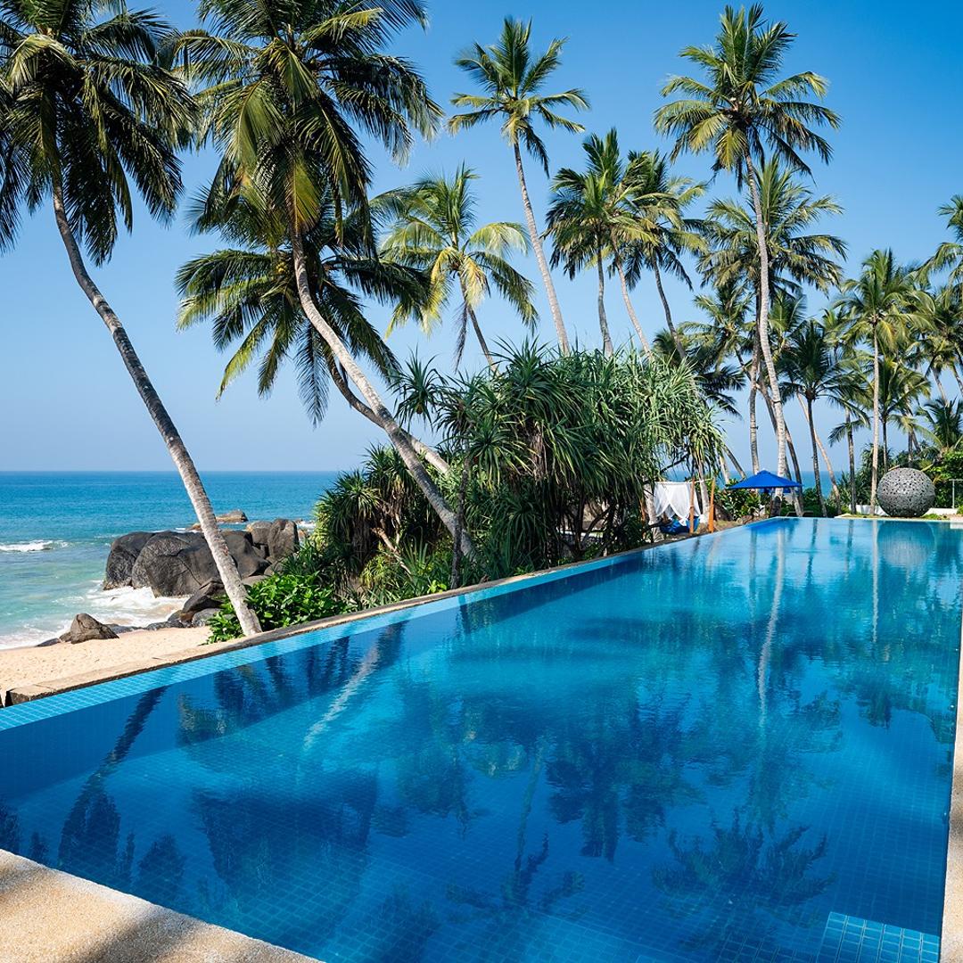 Kumu Beach infinity pool with vivid blue water, palm trees and tropical blue sky