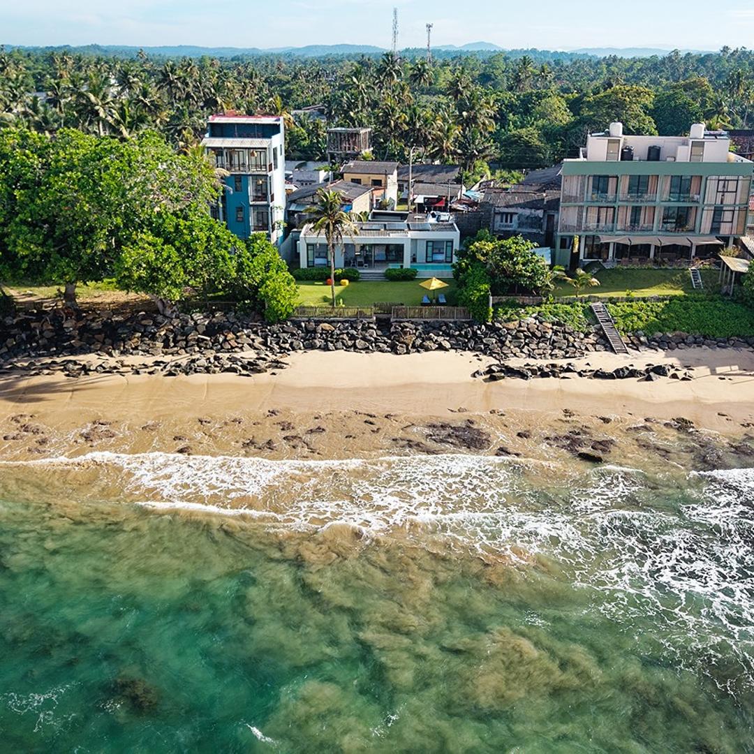 Aerial view of Shoreline Ahangama on rocky beach with coastal town beyond