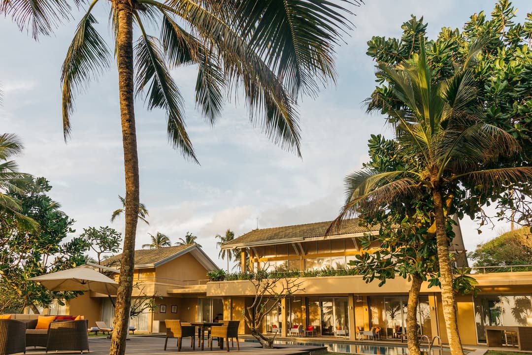Luxury beach villa exterior with mature tropical garden and palm-lined driveway