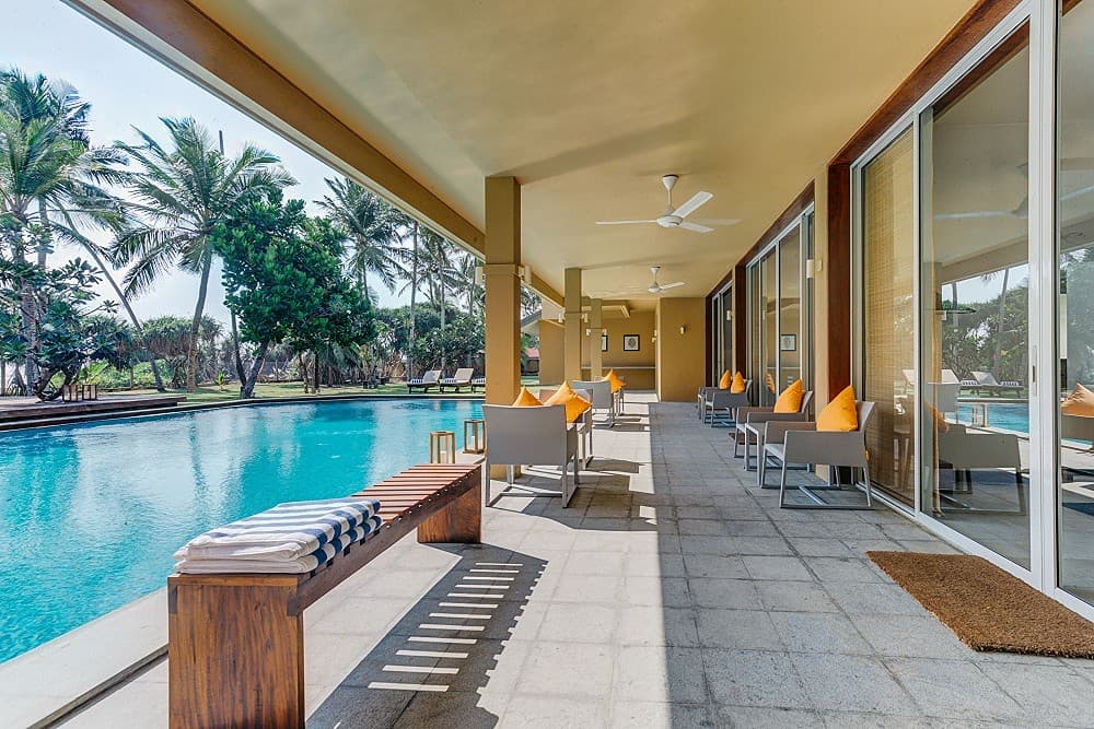 Villa patio with poolside dining table and umbrellas set in a tropical garden