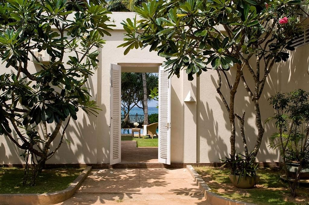 Beachfront villa white facade framed by tropical trees and garden in Induruwa