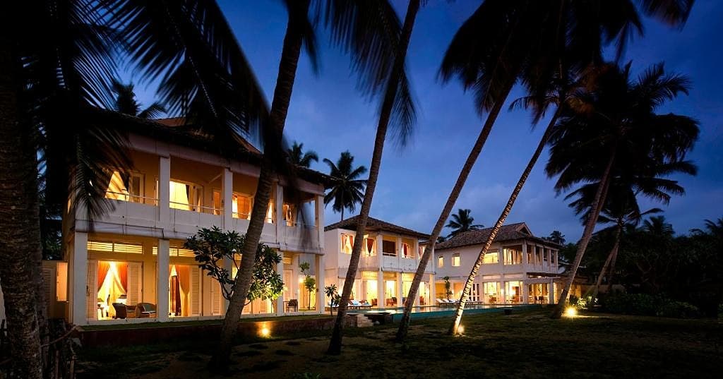 Sri Villas Induruwa exterior illuminated at night with palm trees and warm lighting