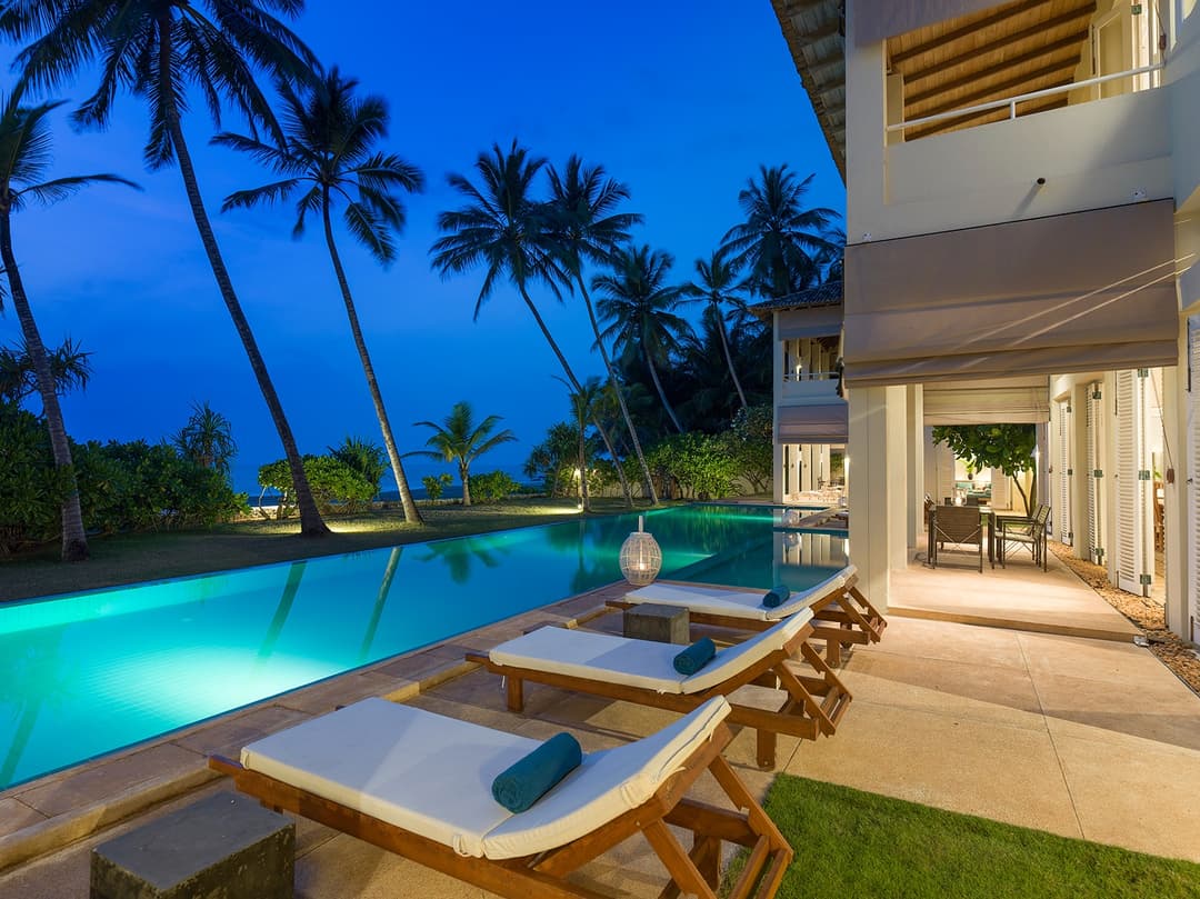 Sri Villas Induruwa infinity pool illuminated at night with lush tropical garden