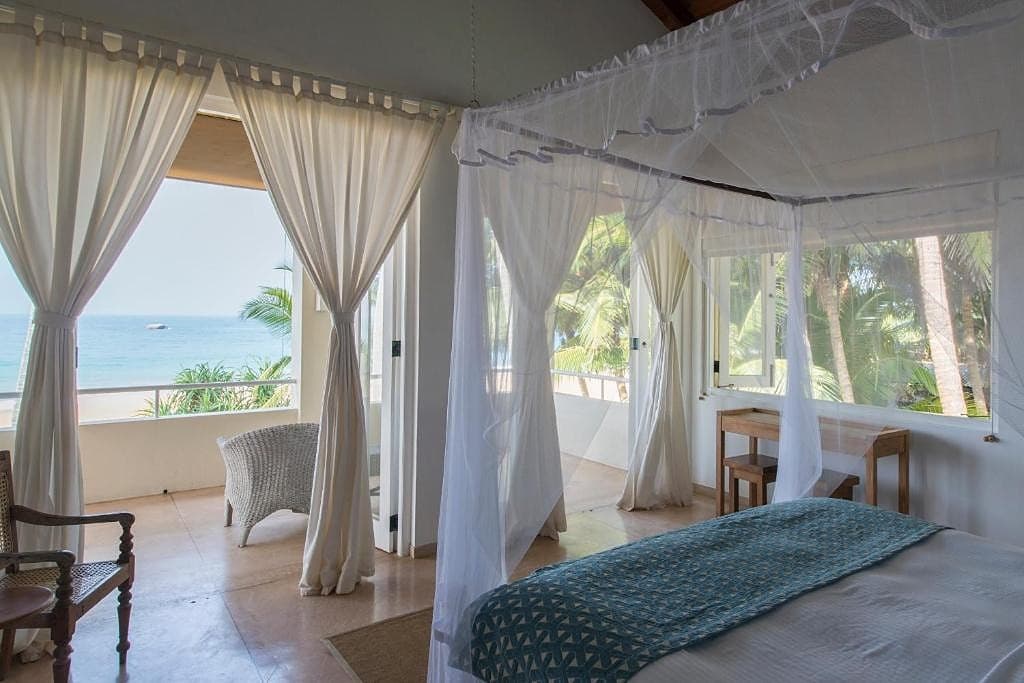 Four-poster bed with draped white canopy and ocean view in a villa at Induruwa