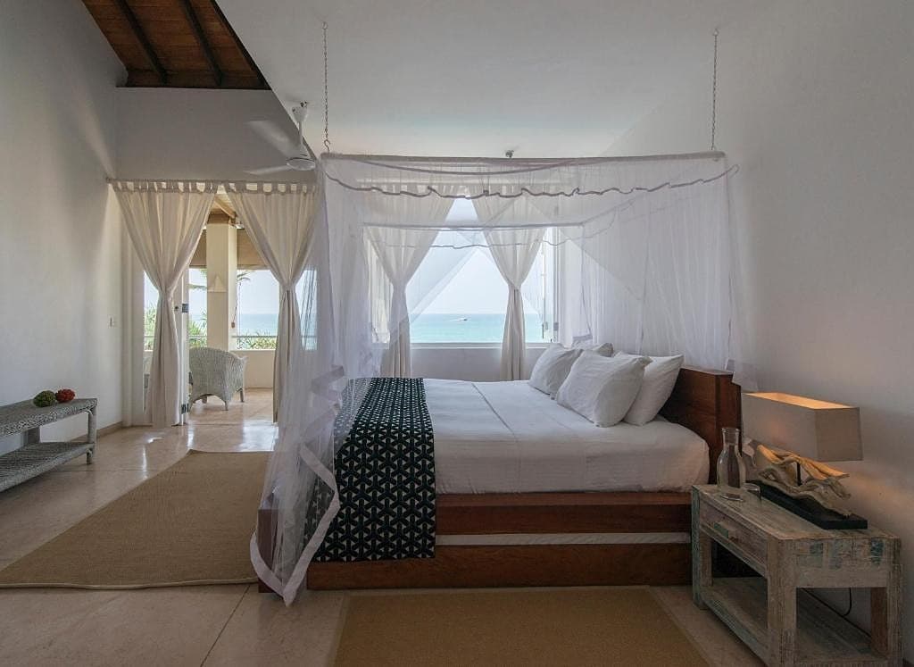 Villa king bedroom with white coastal decor, natural light and shuttered windows