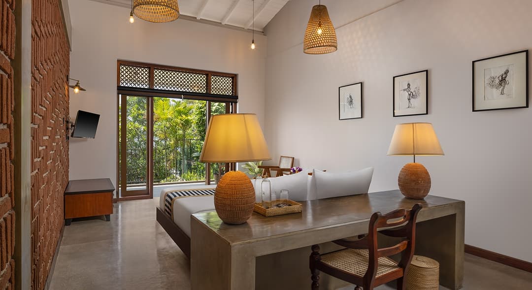 Villa bedroom with timber desk, table lamp and lush tropical garden view