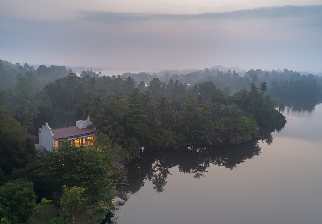 Yahva Bentota villa viewed from Dedduwa Lake through trees at pink dusk