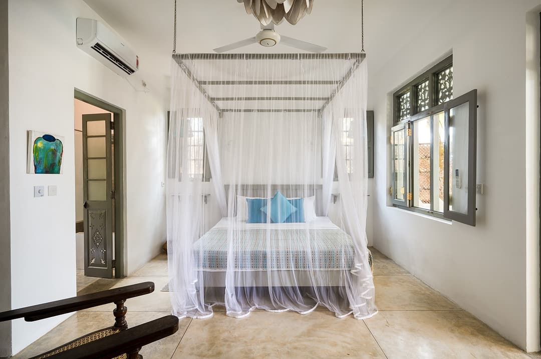 Beachfront villa bedroom with mosquito-net four-poster canopy and garden door