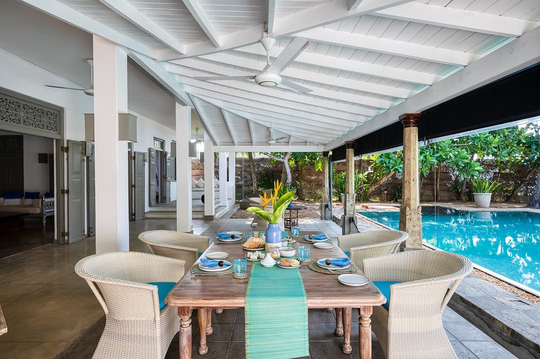 Beachfront villa outdoor dining pavilion with wicker chairs and garden view