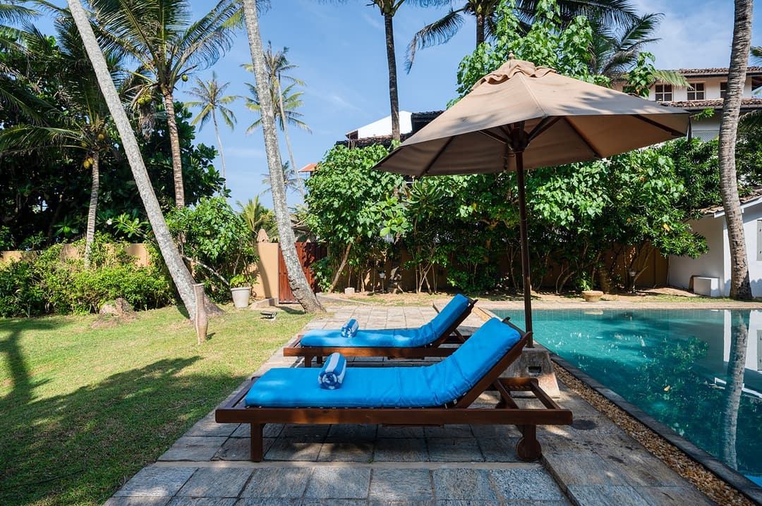 Villa Bleu Unawatuna pool with blue sun loungers and umbrella under coconut palms
