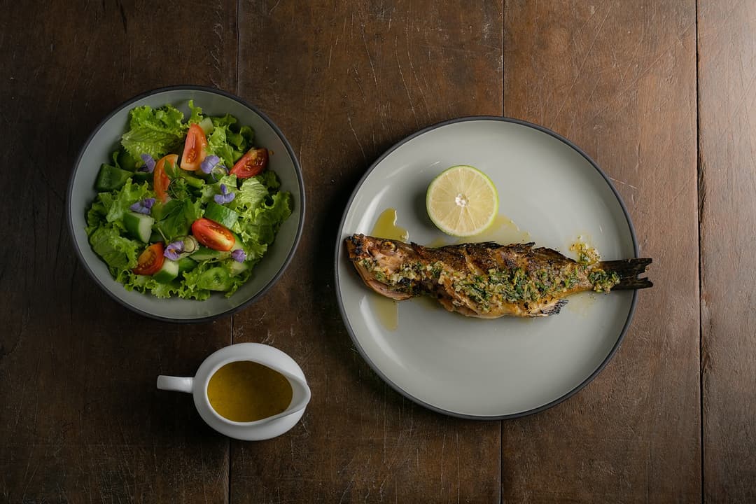 Overhead villa chef grilled fish and salad plates dark table Mirissa