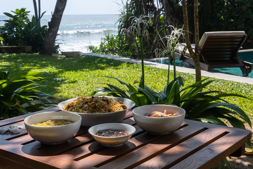 Matara villa outdoor dining with food bowls on pool deck and ocean view