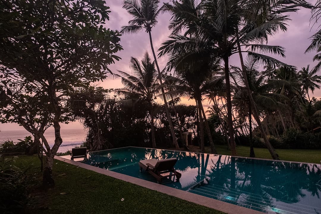 Matara villa pool at sunset with palm tree silhouettes and dramatic sky