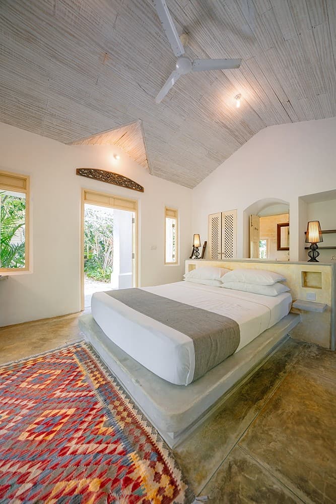 Villa bedroom with white linen and red rug under ceiling fan