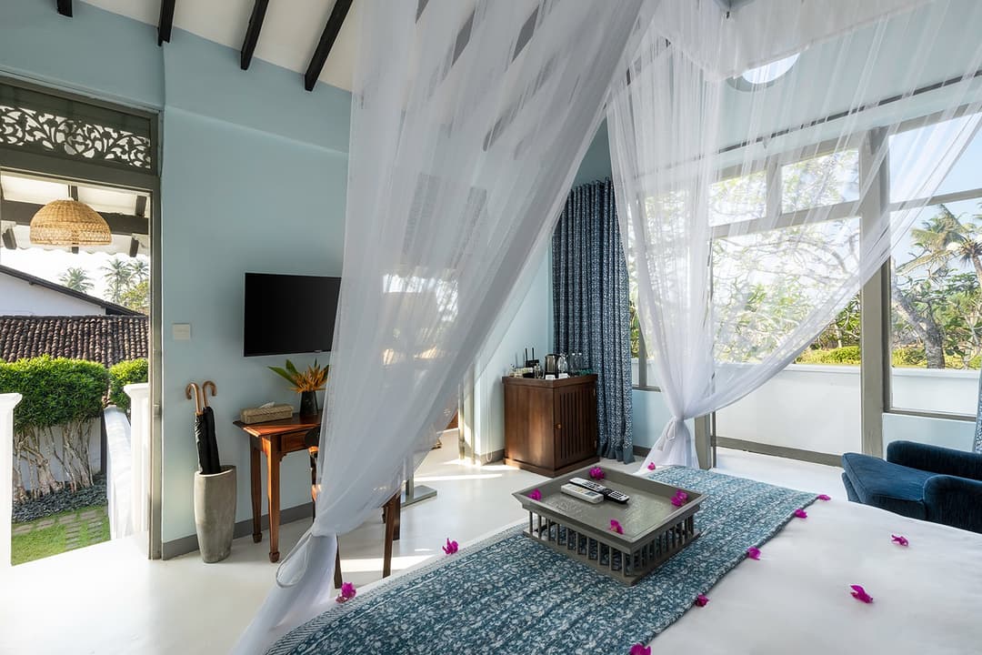 Canopy bedroom with louvred shutters and tropical garden view at Heritage House Bentota