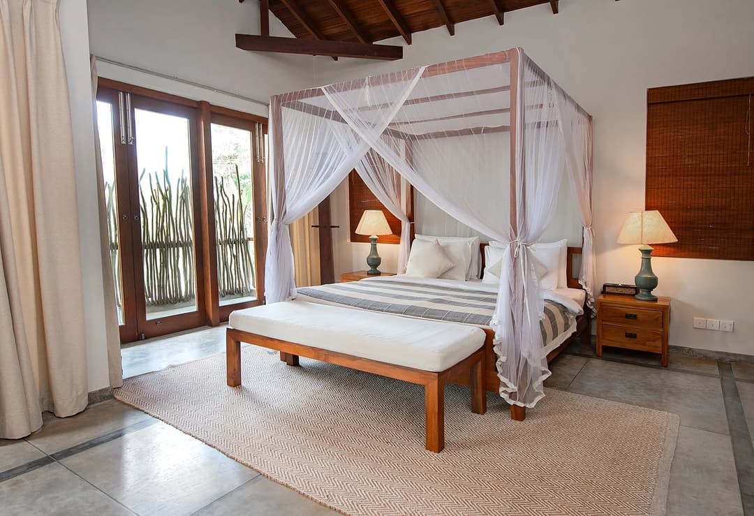 Bedroom with louvred windows and canopy bed at Cottage Kabalana, Ahangama, Sri Lanka