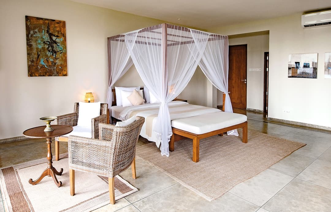 Canopy bedroom with rattan chair and ottoman at Cottage Kabalana, Ahangama, Sri Lanka