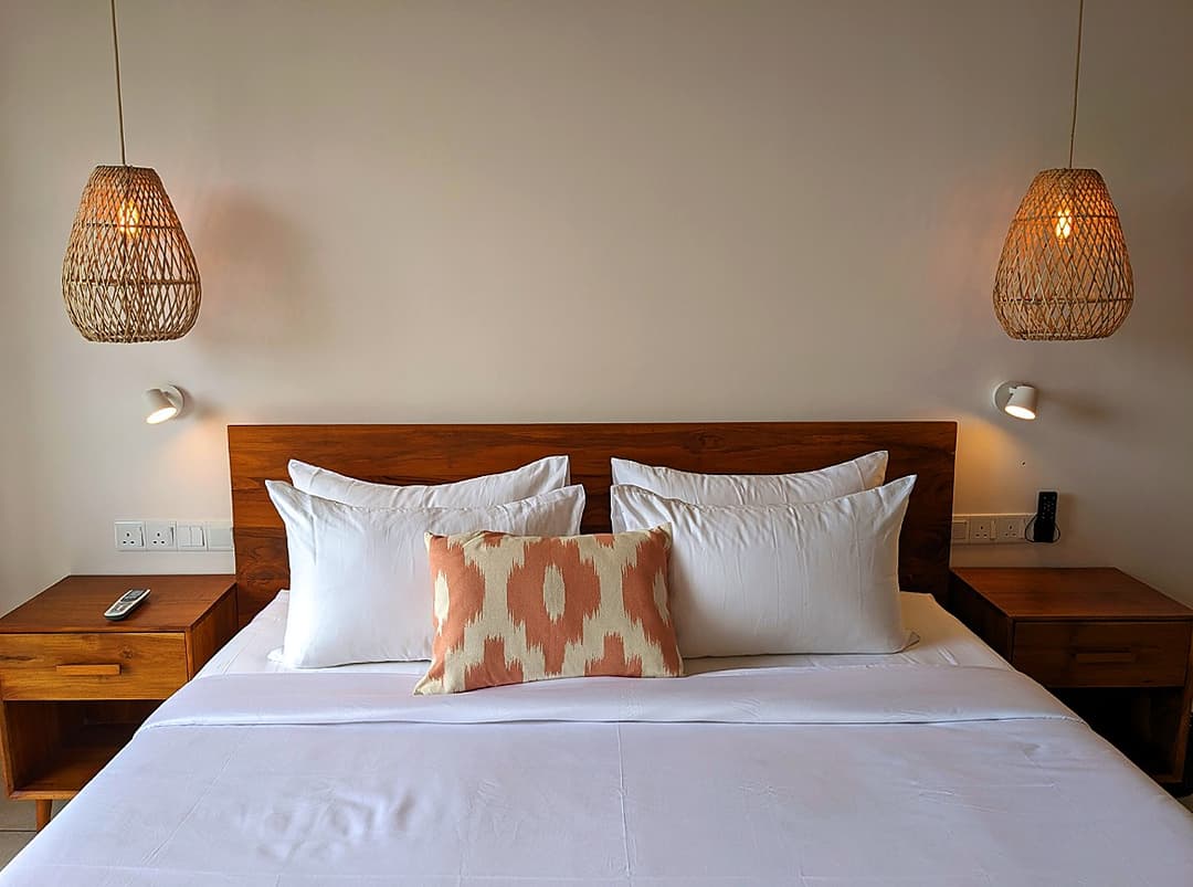 King bedroom with orange accent cushions and rattan lamp at Salt and Stone, Ahangama