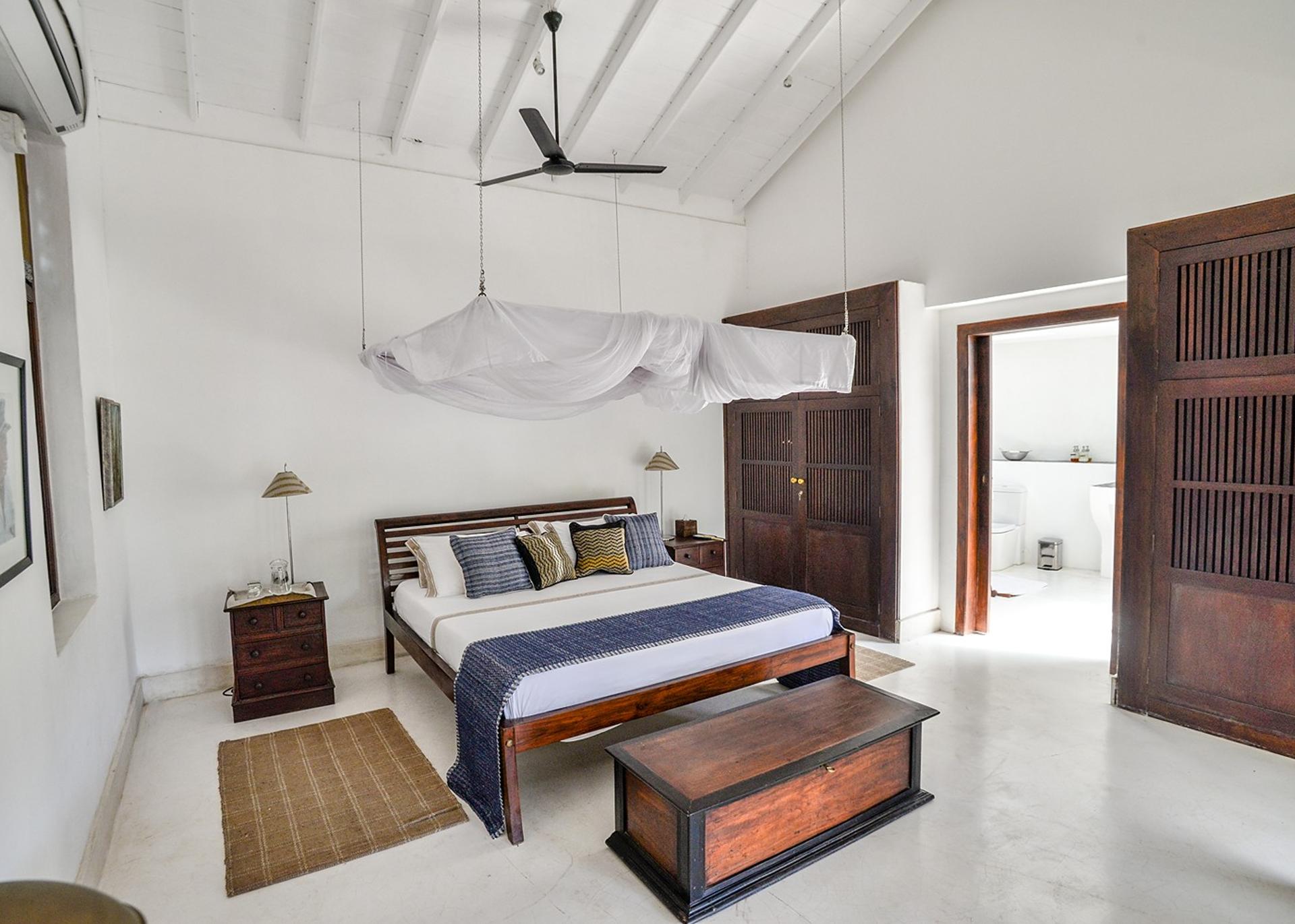 Villa king bedroom with timber shuttered door and blue stripe textile in Galle Fort