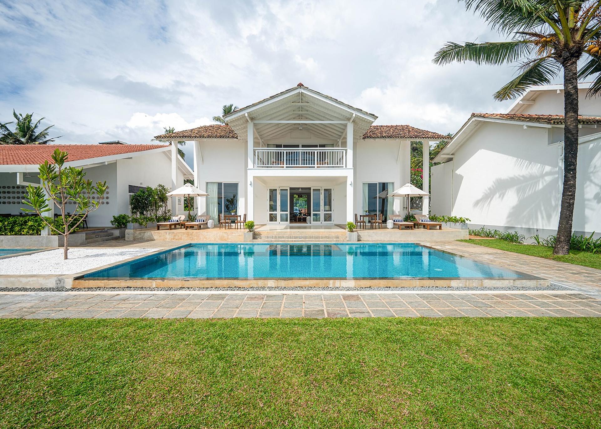 Sol House Mirissa exterior with pool, villa facade and palm trees daytime