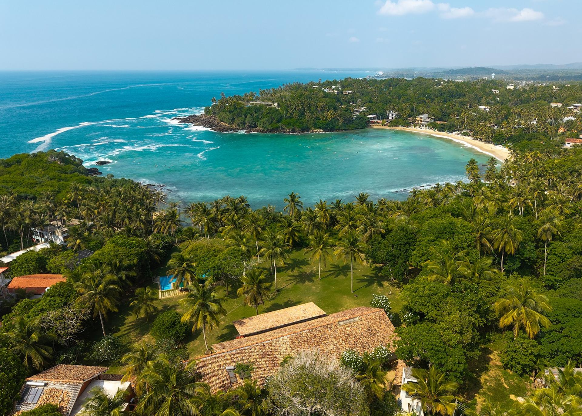 Aerial panorama of Hiriketiya's crescent-shaped beach and turquoise bay, moments from Pavana Hiriketiya villa