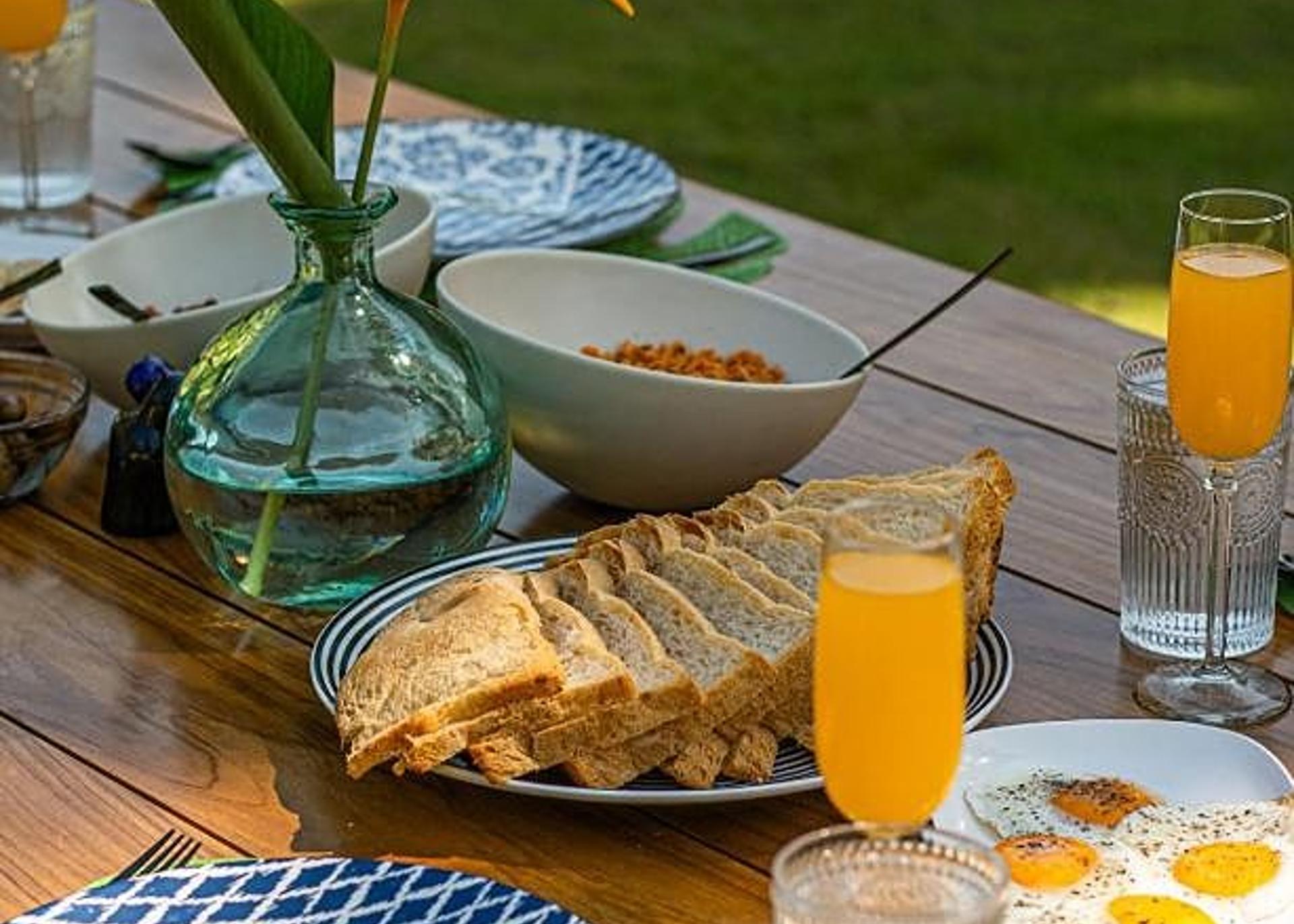 Outdoor breakfast spread on terrace table with tropical garden view