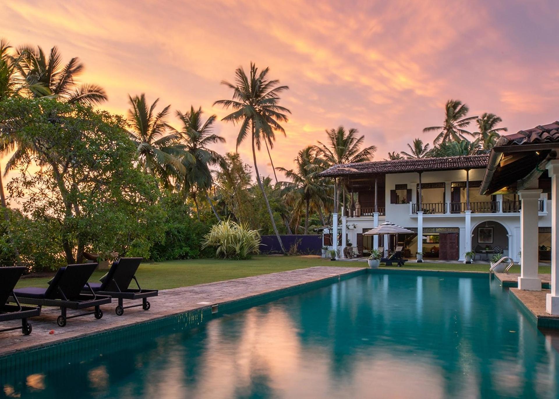Sun loungers beside the pool at dusk with the illuminated villa facade at Casa Lago, Koggala