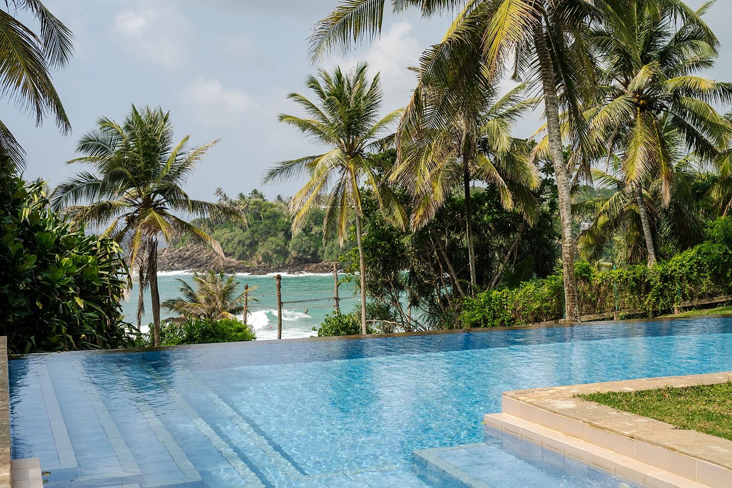 Close-up of the infinity pool edge at Pavana Hiriketiya with lush garden and palm trees in the background