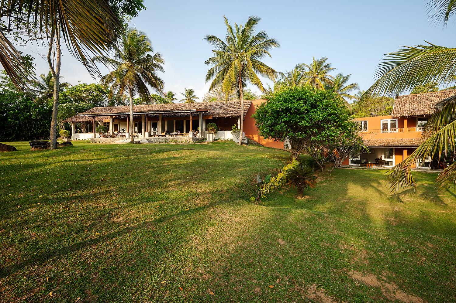 Daytime front view of Pavana Hiriketiya main house with a sprawling front lawn and mature tropical trees